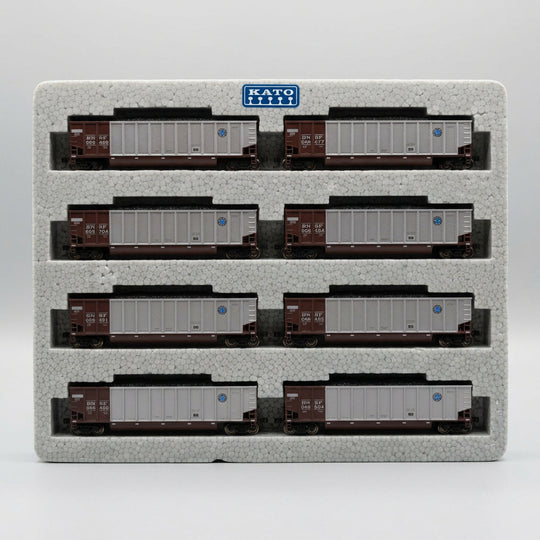 Six N-scale model freight cars arranged in two rows on a gray foam display block, photographed from above on a tan textured surface.